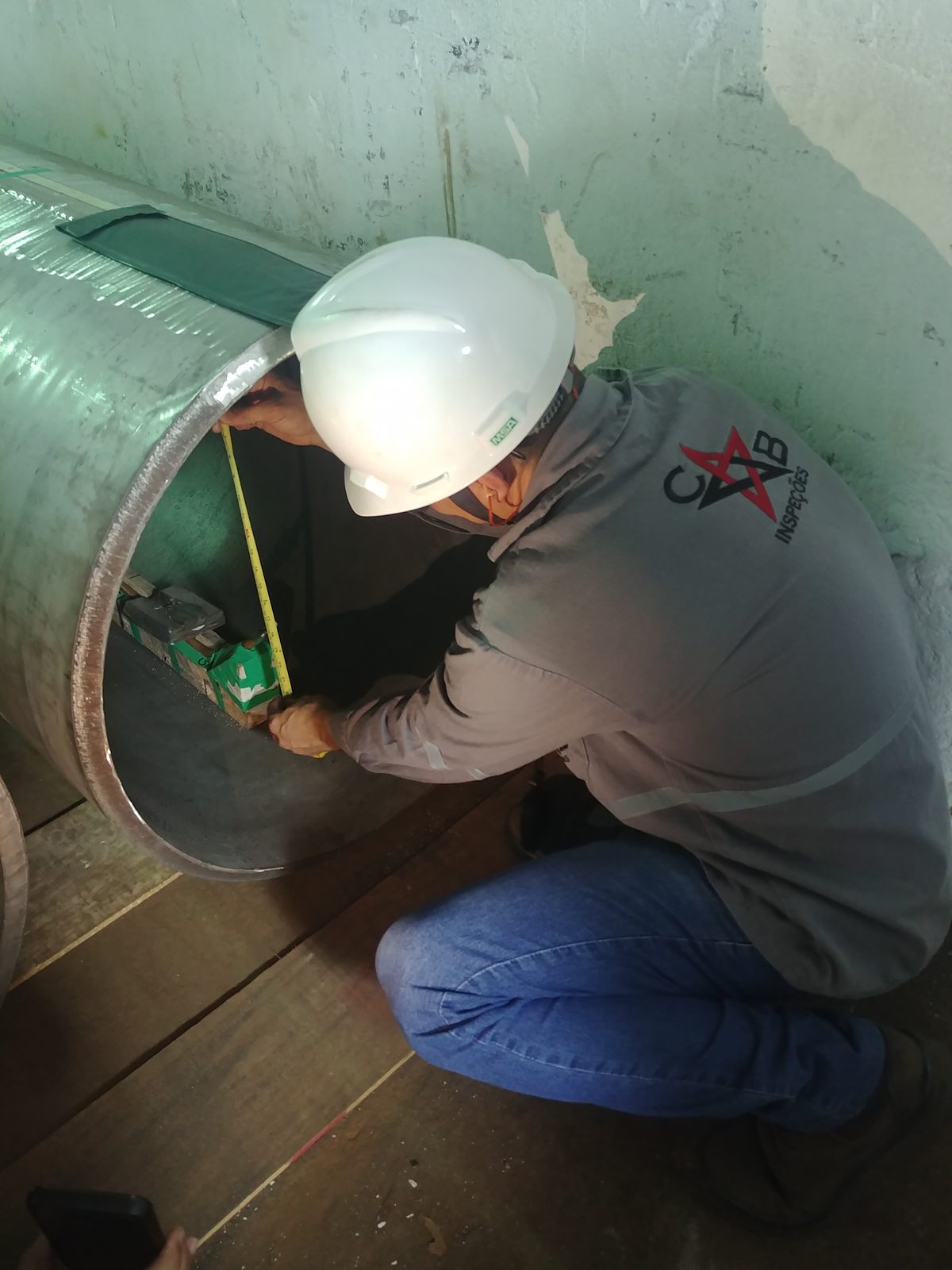 Inspetor da CB Inspeções, de capacete e uniforme, medindo a parede de um tubo antes do ensaio radiográfico