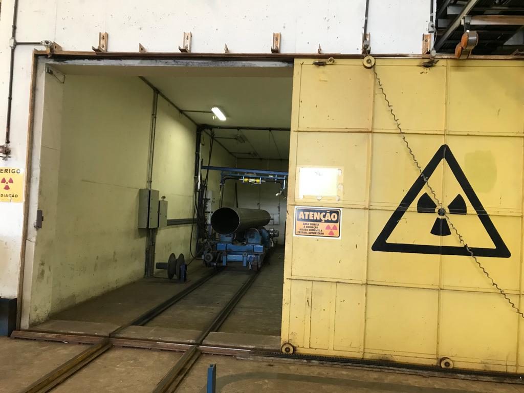 Porta blindada do bunker de radiografia da CB Inspeções com o símbolo de radiação ionizante e placa de atenção